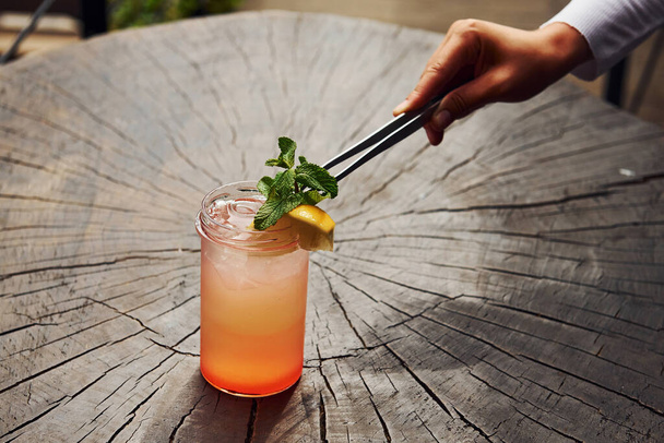 A mão do empregado. Com limão e hortelã. Vista de perto do coquetel alcoólico fresco de verão na mesa de madeira. - Foto, Imagem