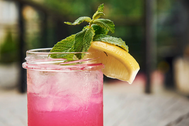 Pink colored liquid with lemon. Close up view of fresh summer alcoholic cocktail on the wooden table. - Foto, Imagem