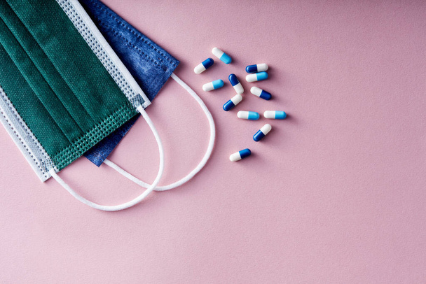 Kilka tabletek i kapsułek doustnych na jednorazowej masce medycznej na różowym tle.  - Zdjęcie, obraz