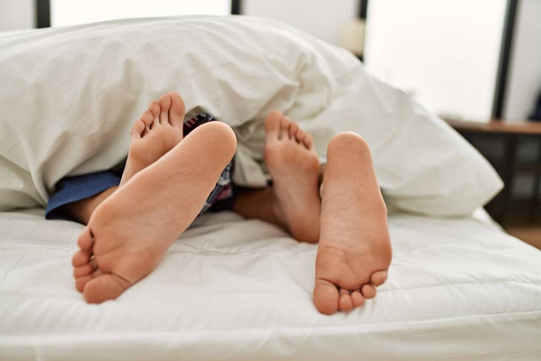 Couple feet under sheets on the bed at home. - 写真・画像