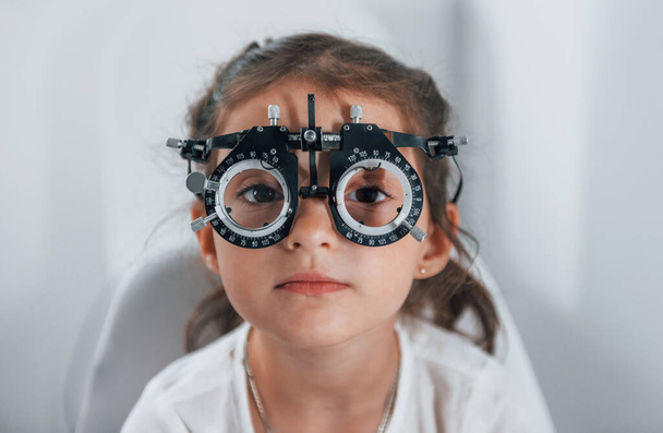 Cute little girl is in ophthalmology clinic with special tool on eyes getting tested. - Foto, Imagem