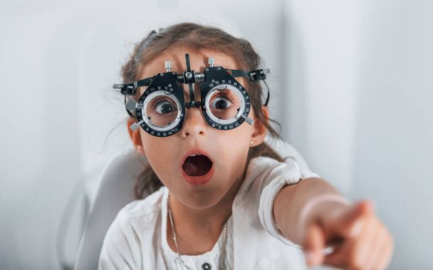 Cute little girl is in ophthalmology clinic with special tool on eyes getting tested. - Foto, Imagen