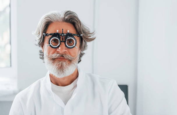 Senior man with grey hair and beard is in ophthalmology clinic. - 写真・画像