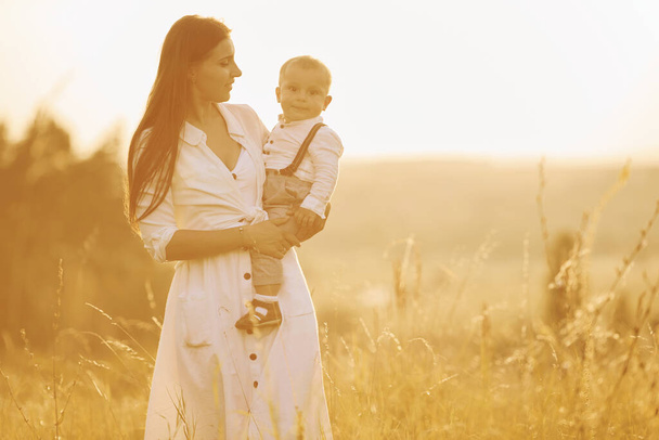 Young mother with her little son is outdoors in the agricultural field. Beautiful sunshine. - Photo, Image