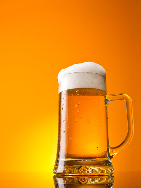 Vaso de cerveza en primer plano con espuma sobre fondo naranja
 - Foto, imagen