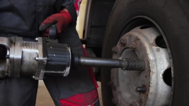 Człowiek z pomocą przemysłowego narzędzia skręca śruby koła z transportu towarowego - Materiał filmowy, wideo