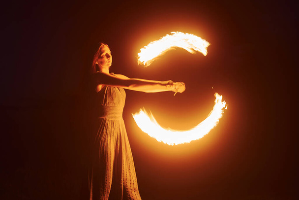 woman performer twirl burning baton during fire performance in dark night outdoors - Foto, imagen