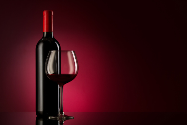 Flasche mit Rotwein und Glas auf rotem Gefälle - Foto, Bild