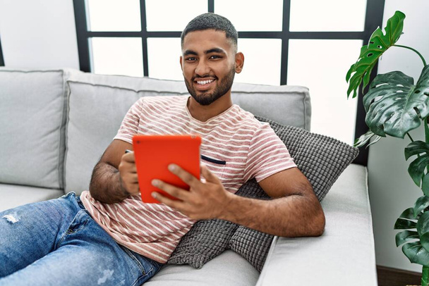 Giovane arabo uomo sorridente fiducioso utilizzando touchpad a casa - Foto, immagini