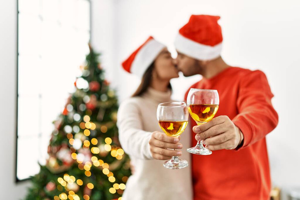 若いですヒスパニックカップル接吻とトーストとともにシャンパン立ってクリスマスツリーにホーム. - 写真・画像