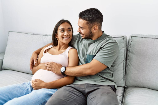Latin erkek ve kadın çift evde bebek beklerken birbirlerine sarılıyorlar. - Fotoğraf, Görsel