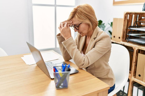 Middelbare leeftijd blonde vrouw werken met ernstige expressie op kantoor - Foto, afbeelding