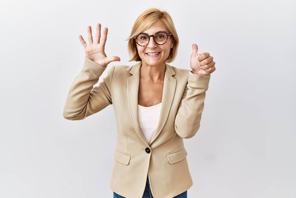 Middle age blonde business woman standing over isolated background showing and pointing up with fingers number six while smiling confident and happy.  - Foto, Bild
