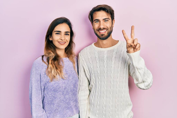 Gündelik kıyafetler giyen genç İspanyol çift iki numarayı gösterip işaret ederken kendinden emin ve mutlu bir şekilde gülümsüyor..  - Fotoğraf, Görsel