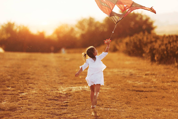 Klein meisje in witte kleren lopen met vlieger buiten op het veld. - Foto, afbeelding