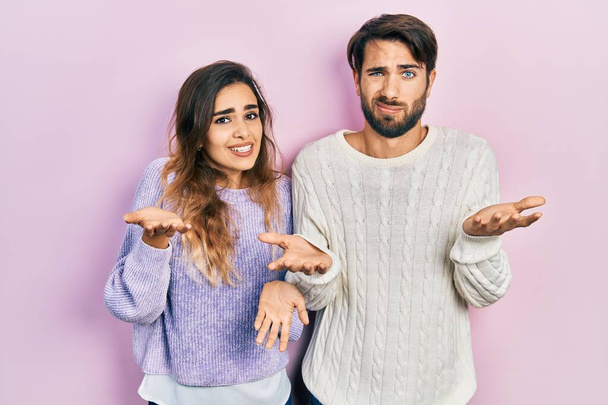 Νεαρό ζευγάρι ισπανόφωνων που φορούν casual ρούχα ανίδεοι και μπερδεμένοι με ανοιχτές αγκάλες, καμία ιδέα.  - Φωτογραφία, εικόνα