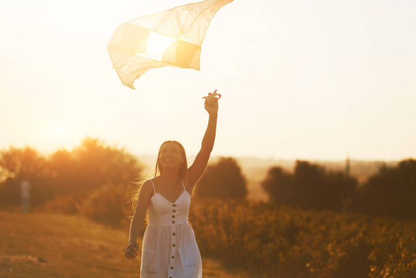 Cheerful woman having fun with kite outdoors on the field at summertime and smiles. - Foto, Imagem
