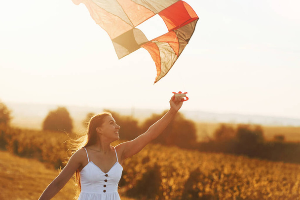 Cheerful woman having fun with kite outdoors on the field at summertime and smiles. - Fotoğraf, Görsel