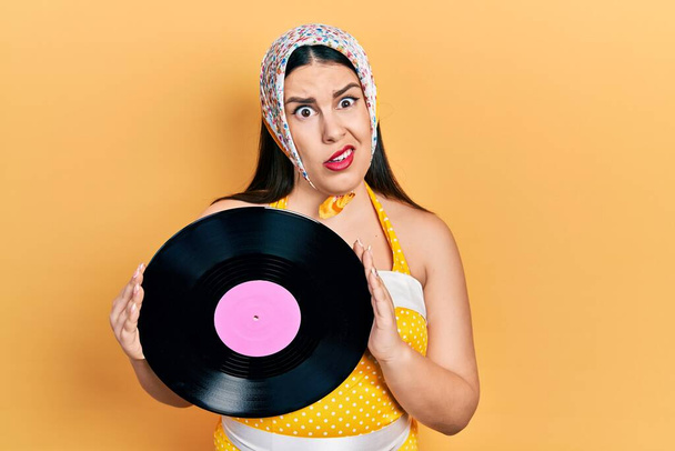 Fiatal spanyol nő tűvel feltűzött stílusban tartja vinyl lemez tudatlan és zavaros kifejezés. kétség.  - Fotó, kép