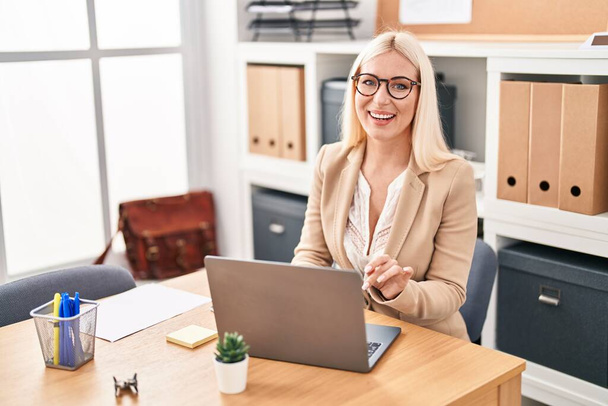 Jonge blonde vrouw zakenman met behulp van laptop werken op kantoor - Foto, afbeelding