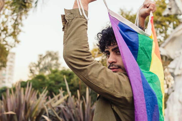 zadní pohled na bělocha venku, držícího vlajku homosexuální hrdosti, hledícího do kamery. - Fotografie, Obrázek