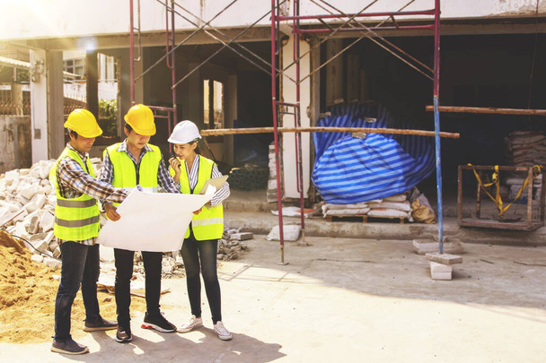 Bayan mimarlar ve erkek işçiler inşaat alanının önündeki projeye göre yenilemeyi planlamak için planlar üzerinde danışmanlık yapıyorlar.. - Fotoğraf, Görsel