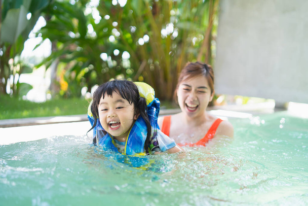 Mère et fille nagent en jouant dans la piscine, souriant et riant. S'amuser dans la piscine de l'hôtel de villégiature, concept familial heureux. - Photo, image