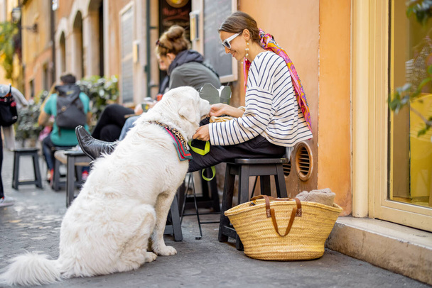 Жінка піклується про свого собаку під час їжі макаронних виробів у відкритому кафе
 - Фото, зображення