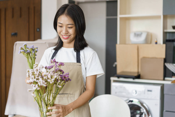 Concept de style de vie à la maison, jeune femme organiser des fleurs pour décorer dans un vase sur la table dans la salle de cuisine. - Photo, image
