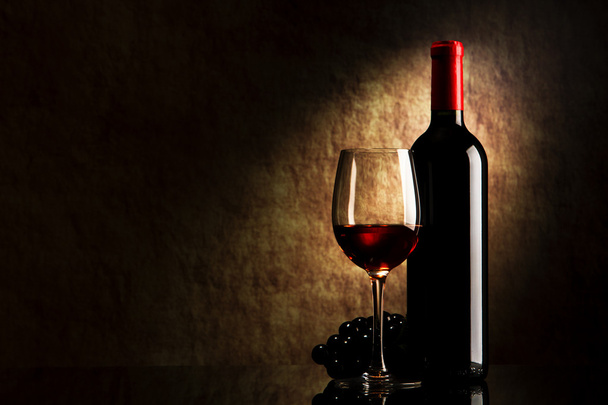 fles met rode wijn en glas en druiven op een oude steen - Foto, afbeelding