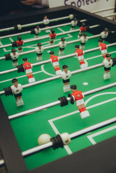 ποδοσφαιρικό τραπέζι, ομάδες ντυμένες με ασπρόμαυρες και κόκκινες και λευκές στολές "παίζουν" στο πράσινο γήπεδο, κατακόρυφα - Φωτογραφία, εικόνα
