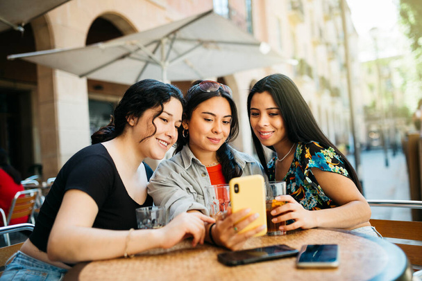 Три молодые женщины делают селфи с телефоном на террасе ресторана - Фото, изображение