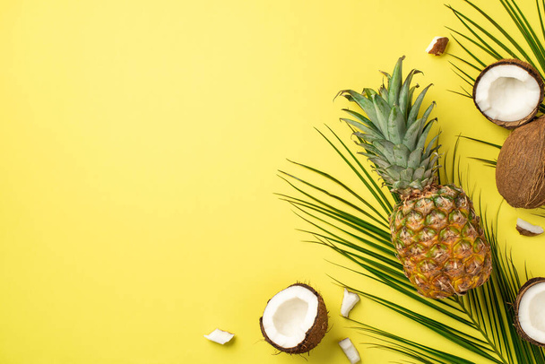 Koncept letního víkendu. Horní pohled fotografie čerstvého tropického ovoce kokosové ořechy ananas a palmové listy na izolovaném žlutém pozadí s copyspace - Fotografie, Obrázek