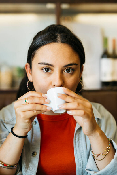 Portret van een jonge Latijnse vrouw die een expresso koffie drinkt in een bar - Foto, afbeelding