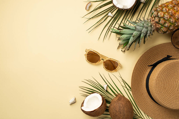Summer holidays concept. Top view photo of headwear sunglasses tropical fruits cracked coconuts pineapple and green palm leaves on isolated beige background - Photo, Image