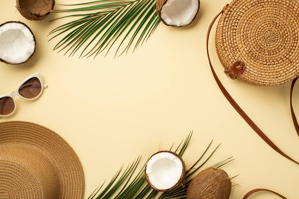 Summer holidays concept. Top view photo of sunhat sunglasses round rattan bag cracked coconuts and green palm leaves on isolated beige background with copyspace in the middle - Foto, imagen