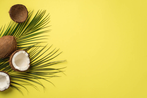 Zomervakantie concept. Bovenaanzicht foto van gebarsten kokosnoten en groene palmbladeren op geïsoleerde gele achtergrond met kopieerruimte - Foto, afbeelding