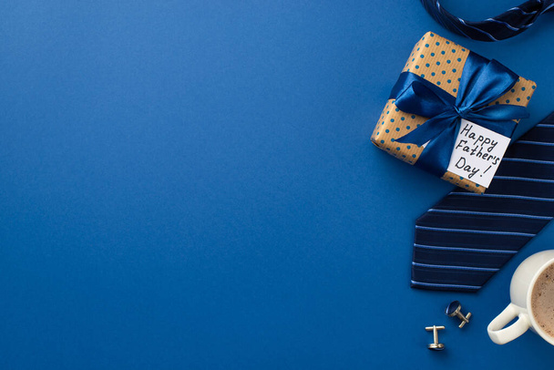 Concepto del Día del Padre. Foto vista superior de la caja de regalo de lunares con lazo de cinta de satén y taza de postal de gemelos de café y corbata azul sobre fondo azul aislado con espacio de copia - Foto, Imagen