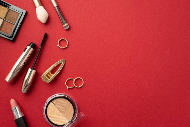 Make-up beauty concept. Top view photo of lipstick contouring eyeshadow palettes mascara makeup brushes gold rings and hairpin on isolated red background with copyspace - Foto, Imagen