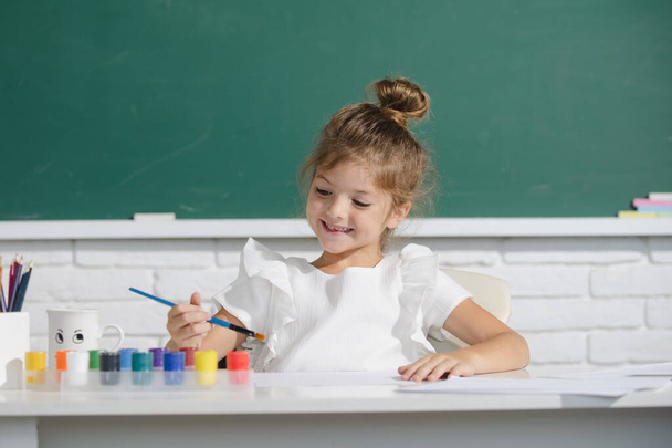 Child girl at school draws with paints. Kids artist creativity. Cute school girl drawing in class at school. - Photo, image
