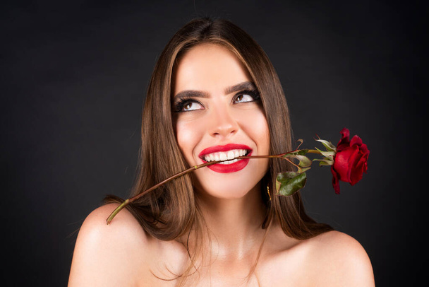 Rose flowers in a womans mouth. Red lips and rose. Beauty girl with sensual mouth. Sexy woman with red rose in teeth on black background. Woman day concept. Happy birthday day. - Photo, image