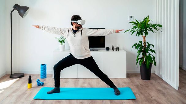 Szakállas férfi VR szemüveges fejhallgatóval és jógázik otthon. Élvezze magával ragadó futurisztikus sportos életmód virtuális valóság. Kiterjesztett valóság, intelligens fitness és innovációs koncepció. - Fotó, kép
