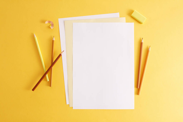 Πολύχρωμα μολύβια, γόμα και άδεια λευκά χαρτιά. Κενό μέρος για κείμενο ή σχέδιο στο κίτρινο φόντο - Φωτογραφία, εικόνα