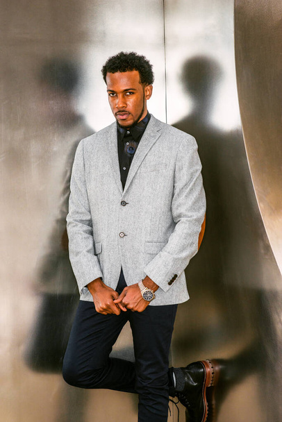 Portret afro-amerykańskiego biznesmena w Nowym Jorku. W szarym wzorzystym blezerze, czarne spodnie, zegarek na rękę, czarny profesjonalista z brodą stojącą przy srebrnej metalowej ścianie.  - Zdjęcie, obraz