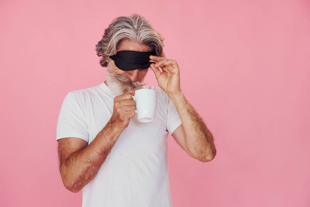 With sleep mask. Waking up. Stylish modern senior man with gray hair and beard is indoors. - Foto, afbeelding