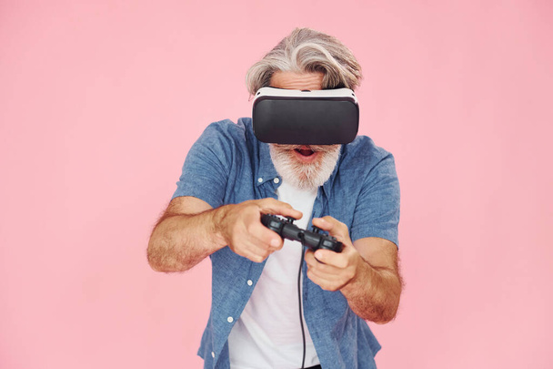 Spiel mit Virtual-Reality-Brille und Joystick. Stilvoller moderner Senior mit grauen Haaren und Bart ist drinnen. - Foto, Bild