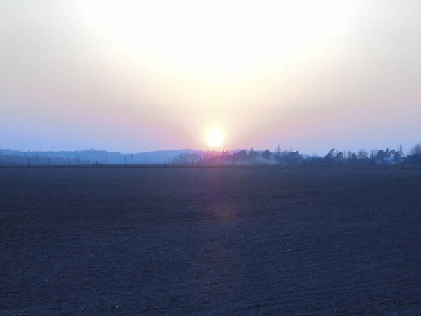 Majestueuse image légèrement surexposée du coucher du soleil créant une lumière massive sur le ciel au-dessus du champ nu et des montagnes au loin. - Photo, image