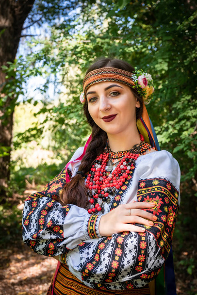 Ουκρανικό κορίτσι σε εθνικό ουκρανικό φόρεμα στέκεται σε ένα μονοπάτι στο δάσος. - Φωτογραφία, εικόνα