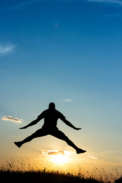 Młody mężczyzna skaczący do wolności, sylwetka w naturze, zachód słońca - Zdjęcie, obraz