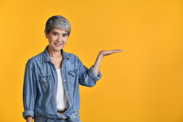 Mujer asiática de mediana edad de 50 años mostrando espacio de copia vacío en la palma de la mano abierta para texto o producto aislado en el fondo de color, mirando y sonriendo a la cámara - Foto, imagen